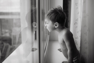 Little caucasian boy looking out the window. Reflection of child face in glass. Image with selective focus