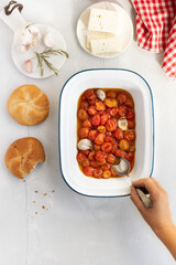 Slow-roasted cherry tomato confit with garlic and rosemary on a tray and accompanied by feta cheese. Trending viral recipe. Top view. White background