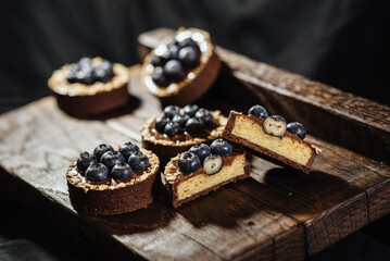 Chocolate tartlets decorated with blueberries on a dark wooden background. Beautiful portion cakes for the holiday table. Dessert with fresh blueberries.