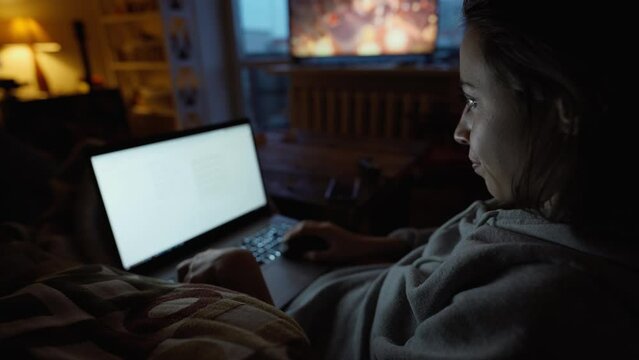 woman sits in dark room at home on couch with laptop, working remotely, shopping online. freelancer, remate work, workplace at home