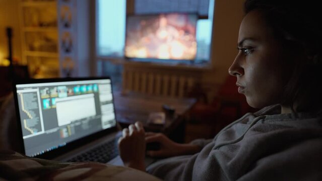 woman sits in dark room at home on couch with laptop, working remotely, shopping online. freelancer, remate work, workplace at home