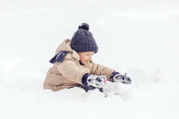 Fototapeta na wymiar Portrait of little happy boy sitting in snow