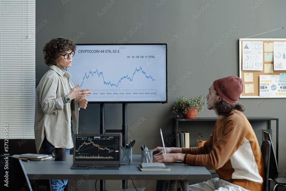 Poster young confident female coach standing by interactive whiteboard with graph illustrating cryptocoin d
