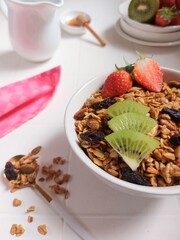 A bowl of granola. Completed with dried fruit, kiwi, strawberry, honey, honey dipper, mug jug, spoon. Healthy food concept. Isolated background in white.