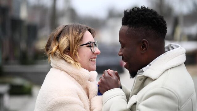 Young african man kisses, warms and blows on hands of caucasian woman.