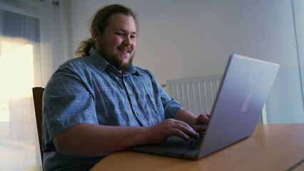 One chubby man in front of laptop working from home. Person browsing internet using computer liking content online celebrating success