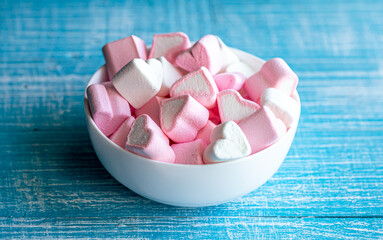 Bowl with marshmallows in the form of hearts on a blue wooden background.