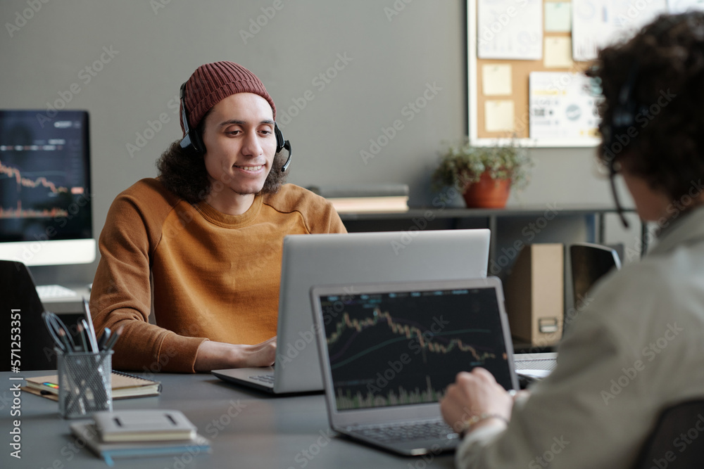 Aufkleber young smiling male operator in headset and casualwear consulting online clients while sitting by wor