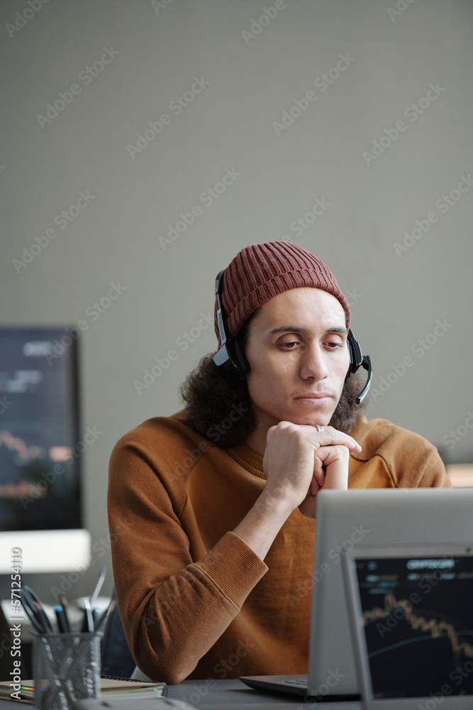 Aufkleber young serious male operator of call center in headset looking at laptop screen by workplace while li