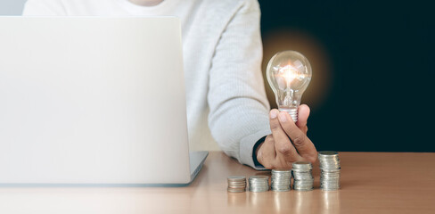 Woman holding light bulb in hand on wooden table in concept of savings, investment, savings and accumulation plan