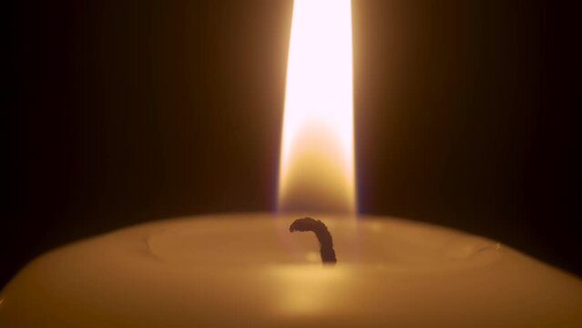 Macro burning candle isolated on black background. Infinitely flame of white paraffin candle in night. Lifestyle remembrance celebration religious