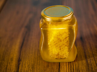 Glass jar of honey with honeycomb inside on a wooden surface,. Selective focus. Top high quality product. Rich golden yellow color.