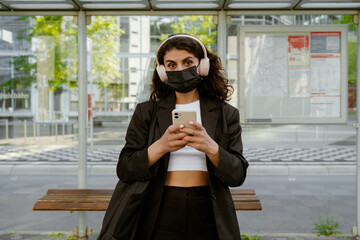 Young businesswoman in face mask listening music and using cellphone