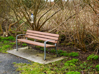 Brown plastic bench with metal frame in a park and a home made DIY bird feeder. Scene in a park. Nobody.