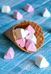 Waffle cone with heart-shaped marshmallows, close-up on a blue wooden background.