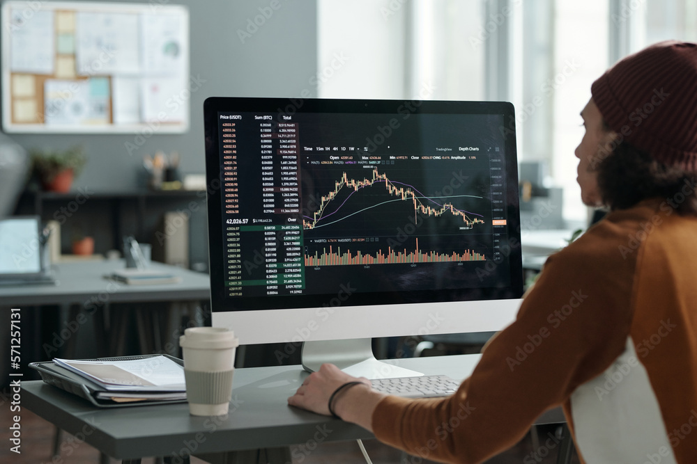 Aufkleber Male analyst sitting in front of computer monitor with graph illustrating development and fluctuations of stock exchange on screen