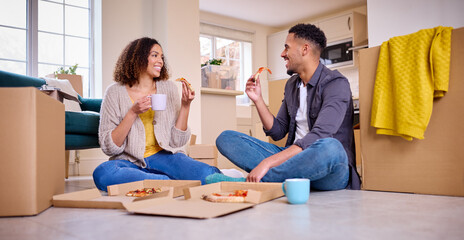 Fototapeta premium Excited Couple Moving Into New Home Celebrating Sitting On Floor Eating Takeaway Pizza