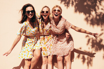 Three young beautiful smiling hipster female in trendy summer dress clothes. Sexy carefree women posing in the street. Positive models having fun outdoors at sunny day. Cheerful and happy. Near wall