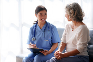 Asian female doctor or nurse gently guide and care for elderly patient at home, giving warm encouragement and consolation.