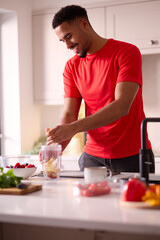 Fototapeta na wymiar Man In Kitchen At Home Wearing Fitness Clothing Blending Fresh Ingredients For Healthy Drink