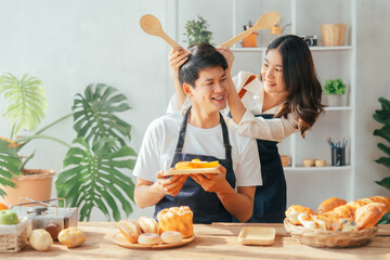 Young Asian couple doing holiday together in the kitchen happily wearing apron. love and valentine concept