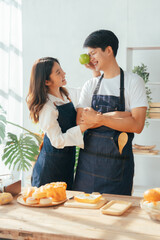 Young Asian couple doing holiday together in the kitchen happily wearing apron. love and valentine concept