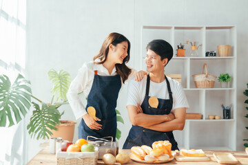 Obraz na płótnie Canvas Young Asian couple doing holiday together in the kitchen happily wearing apron. love and valentine concept