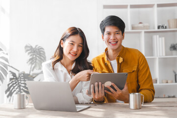 Asian couple husband and wife using laptop and paper bills at home use banking applications sit together at the table A cautious family spouse is confused by high expenses. insurance or rent concept