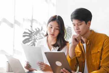 Asian couple husband and wife using laptop and paper bills at home use banking applications sit...