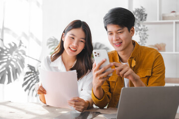 Asian couple husband and wife using laptop and paper bills at home use banking applications sit together at the table A cautious family spouse is confused by high expenses. insurance or rent concept