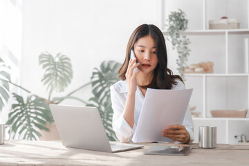 Young pretty asian housewife using laptop with household expenses and financial document on table, work at home concept.