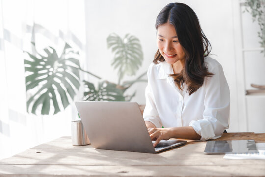 Young pretty asian housewife using laptop with household expenses and financial document on table, work at home concept.