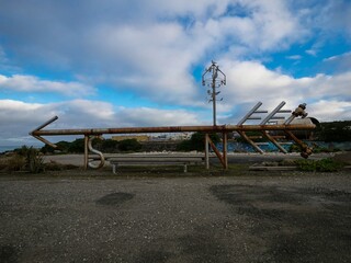 Old rusty pipe arrow shaped industrial art sculpture, navigation direction symbol in gravel car park, Bluff New Zealand