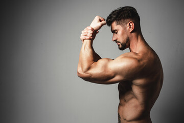 Muscle handsome young man with stylish haircut posing over gray background. Perfect body&skin....