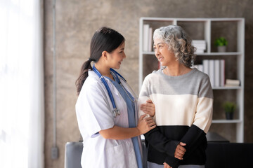 Fototapeta premium Asian female doctor or nurse gently guide and care for elderly patient at home, giving warm encouragement and consolation.