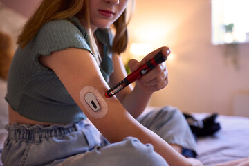 Close Up Of Young Diabetic Girl Sitting On Bed In Bedroom At Home Using Kit To Check Insulin Levels