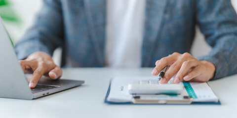 Young asian bookkeepers business man working with paper chart of balance sheet, asset, profit or loss of company with yearly reports. Using calculator