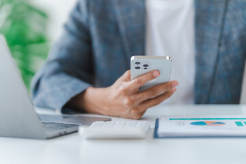 Young asian bookkeepers business man working with paper chart of balance sheet, asset, profit or loss of company with yearly reports. Using mobile smartphones
