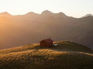 Sunset panorama of red idyllic remote lonely alpine mountain Brewster Hut above Haast valley...
