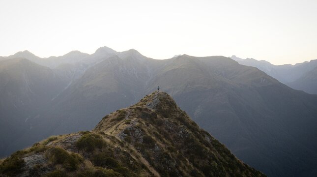 Young female woman hiking along remote alpine mountain ridge path, Brewster Hut Haast Valley, Southern Alps New Zealand