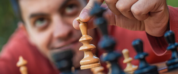 Hand of a man taking a chess piece to make the next move in a chess game. Close up. Spring day...