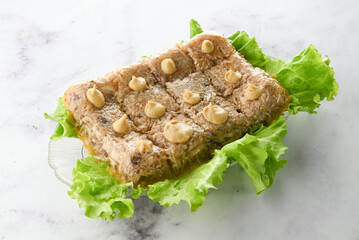Meat jelly decorated with lettuce leaves on a plate on a light background.