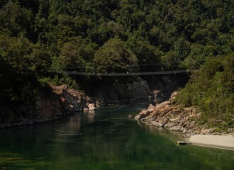 Fototapeta na wymiar Downstream view of multiple people crossing Buller Gorge Swing bridge over Buller River in Murchison Tasman New Zealand