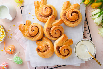 Easter breakfast Holliday concept. Easter bunny buns rolls with cinnamon made from yeast dough with orange glaze, easter decorations, colored eggs on pink spring background. Easter Holliday card.