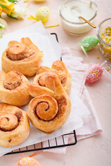 Easter breakfast Holliday concept. Easter bunny buns rolls with cinnamon made from yeast dough with orange glaze, easter decorations, colored eggs on pink spring background. Easter Holliday card.