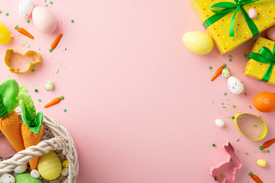 Easter celebration concept. Top view photo of yellow gift boxes basket with colorful easter eggs carrots animal shaped baking molds and sprinkles on isolated pastel pink background with blank space