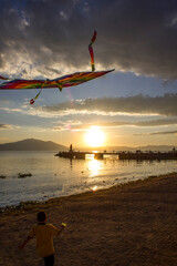 Boy flying a kite on the beach of a lake at sunset
