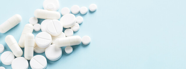 Various white pills on blue background. Banner for concept of medicine and pharmacy.
