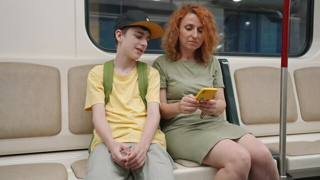 Portrait Young woman with teenager sitting in subway car looking at route on map in smartphone smiling. Mom and son travel in Athens, Greece go underground by train to zoo. Go Everywhere. Travel