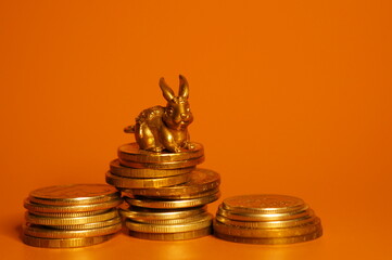 Rabbit figurine with coins on a bright colored background. The symbol of Feng shui. Economics and finance.